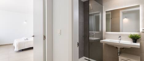 Un baño moderno con cabina de ducha de vidrio, un lavamanos con espejo y un taburete pequeño.