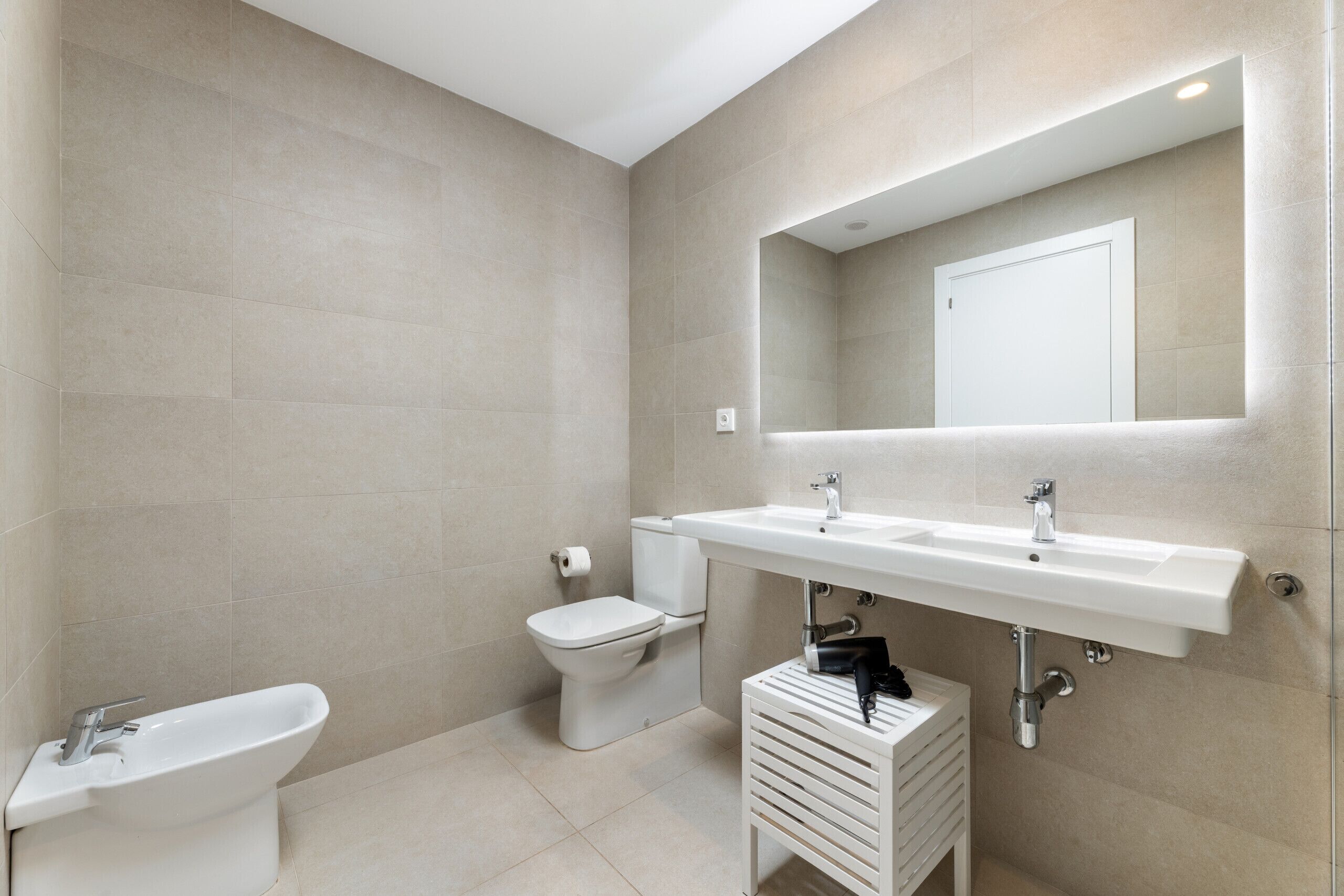 Ein modernes Badezimmer mit einer Bidet-Funktion, Toilette und einem Doppelwaschbecken unter einem Spiegel.