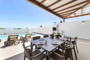 Un espace extérieur abrité, aménagé pour les repas, avec une piscine, des chaises et une table pour quatre personnes.