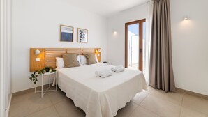 A modern hotel room with a large bed, a bedside table with a plant, a nightstand, and a view of the outdoors. - Villa Los Altos Blanca 8A by Escape Home (Playa Blanca)