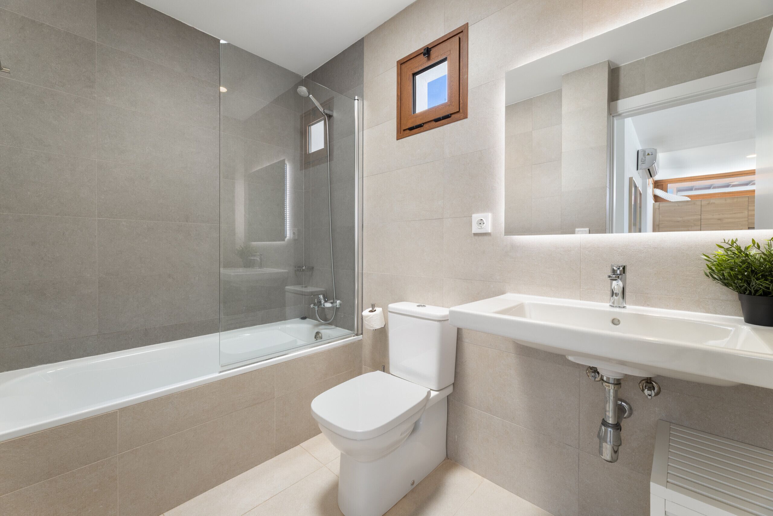 A modern bathroom with a glass-enclosed shower, a white toilet, and a sink with a mirror above it.