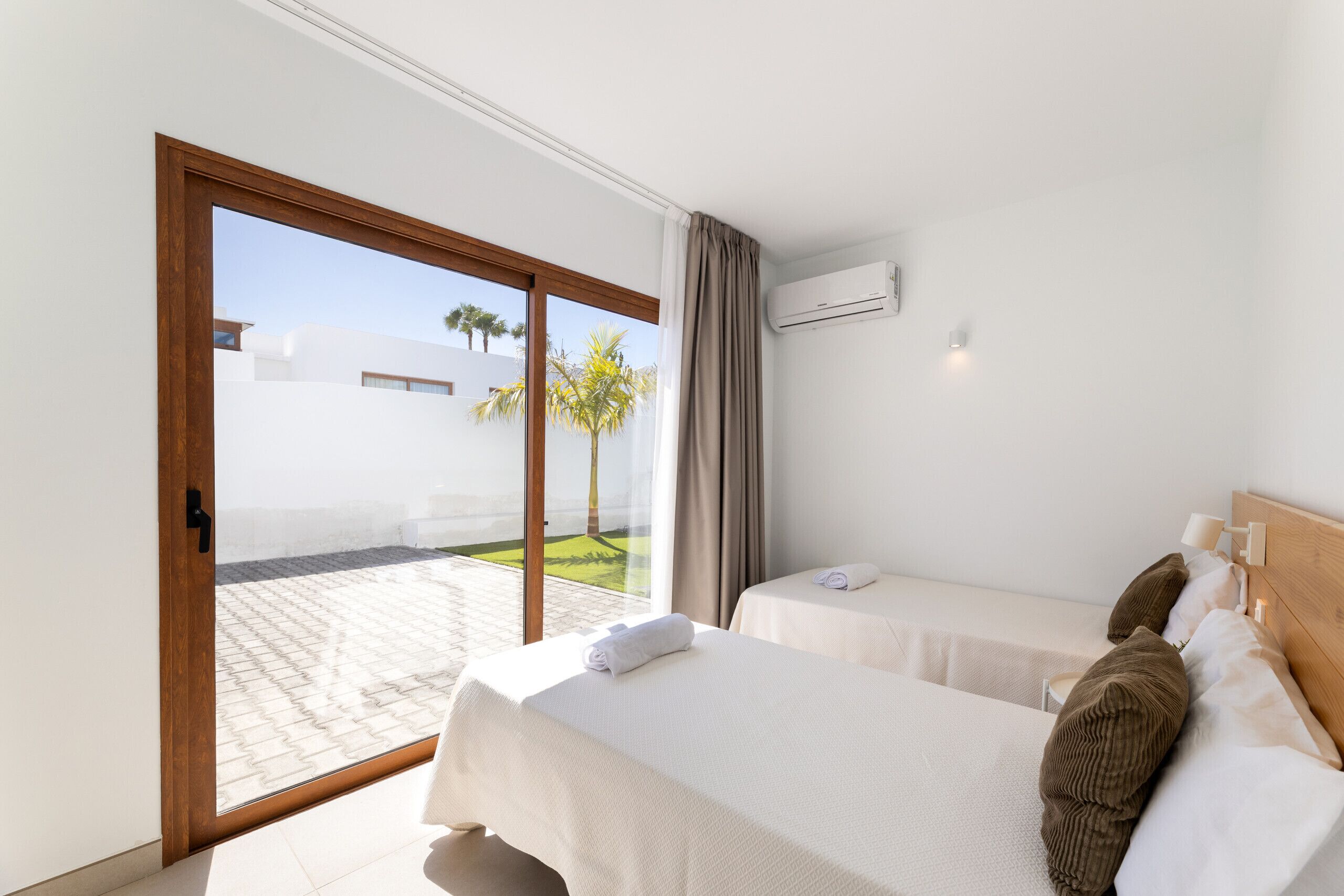 Ein Hotelzimmer mit zwei Betten, einer Schiebetür zum Außenbereich und einer Klimaanlage an der Wand.