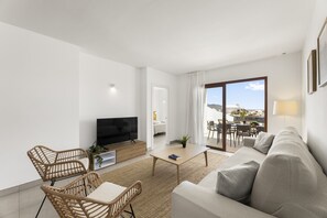 Un salon moderne comprenant un canapé, des fauteuils, un téléviseur et un coin repas avec une table et des chaises.