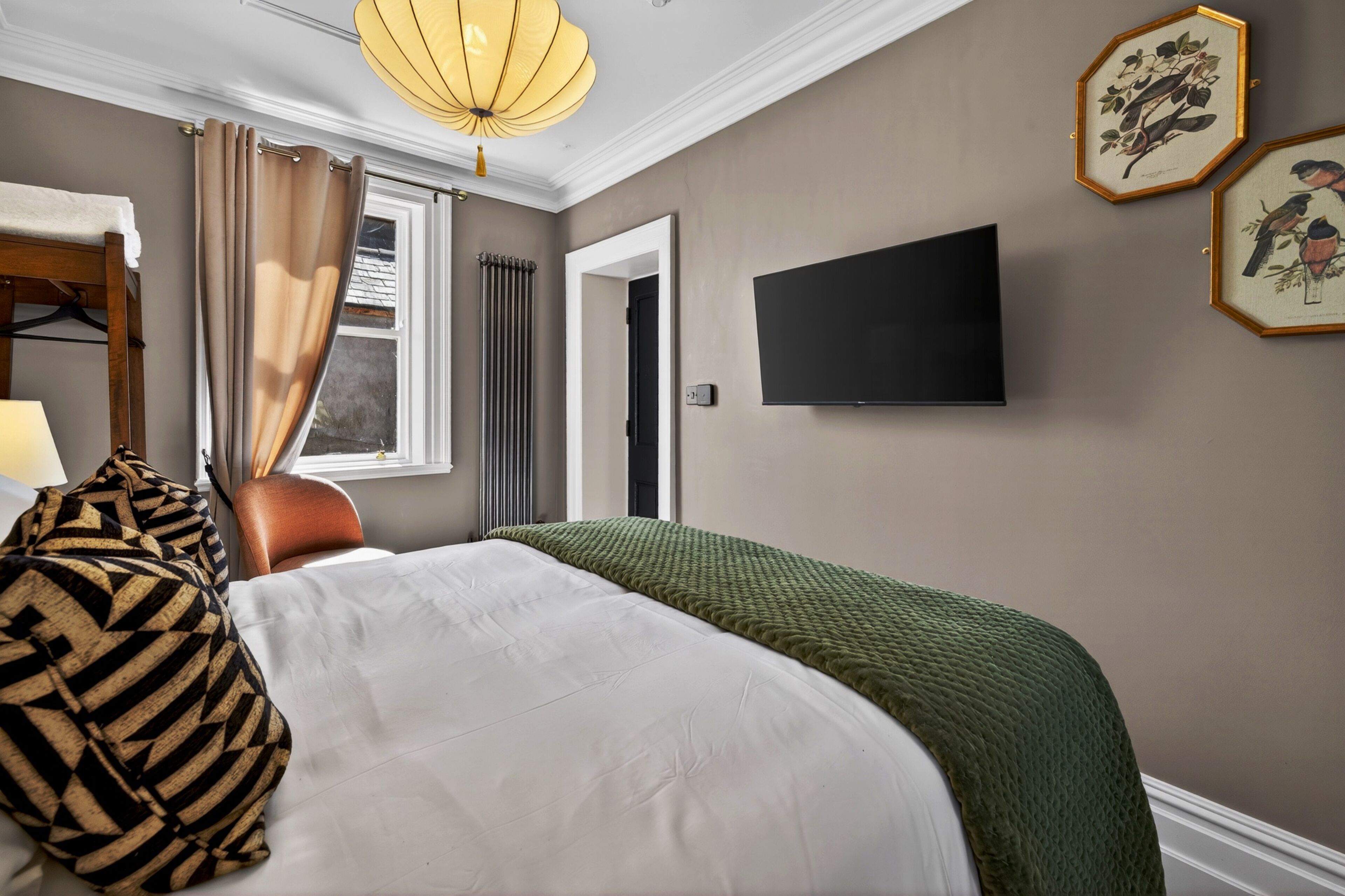 A hotel room with a bed, a television, a window with curtains, and framed artwork on the wall.