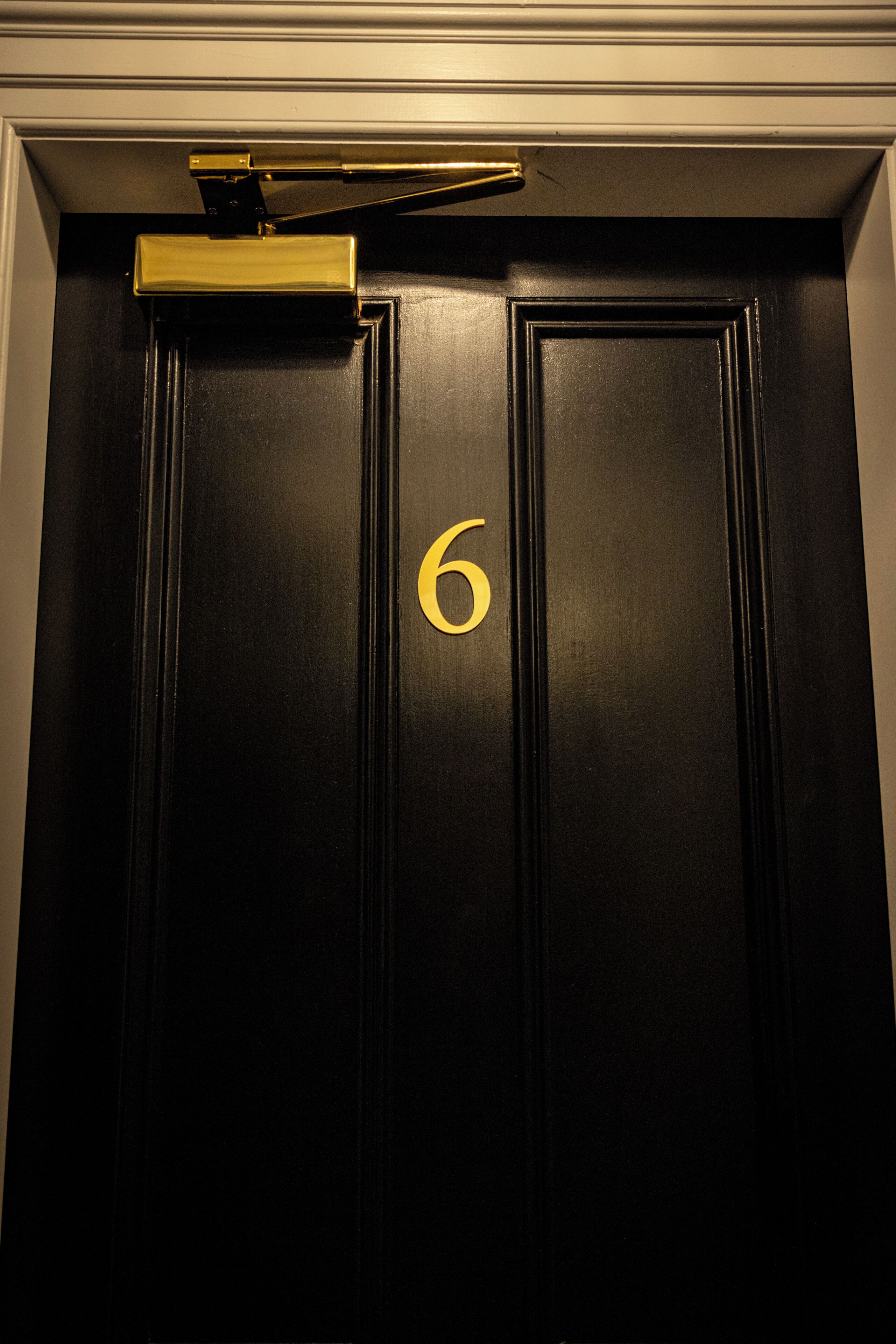 Una porta nera con il numero '6' dorato e un campanello dorato.