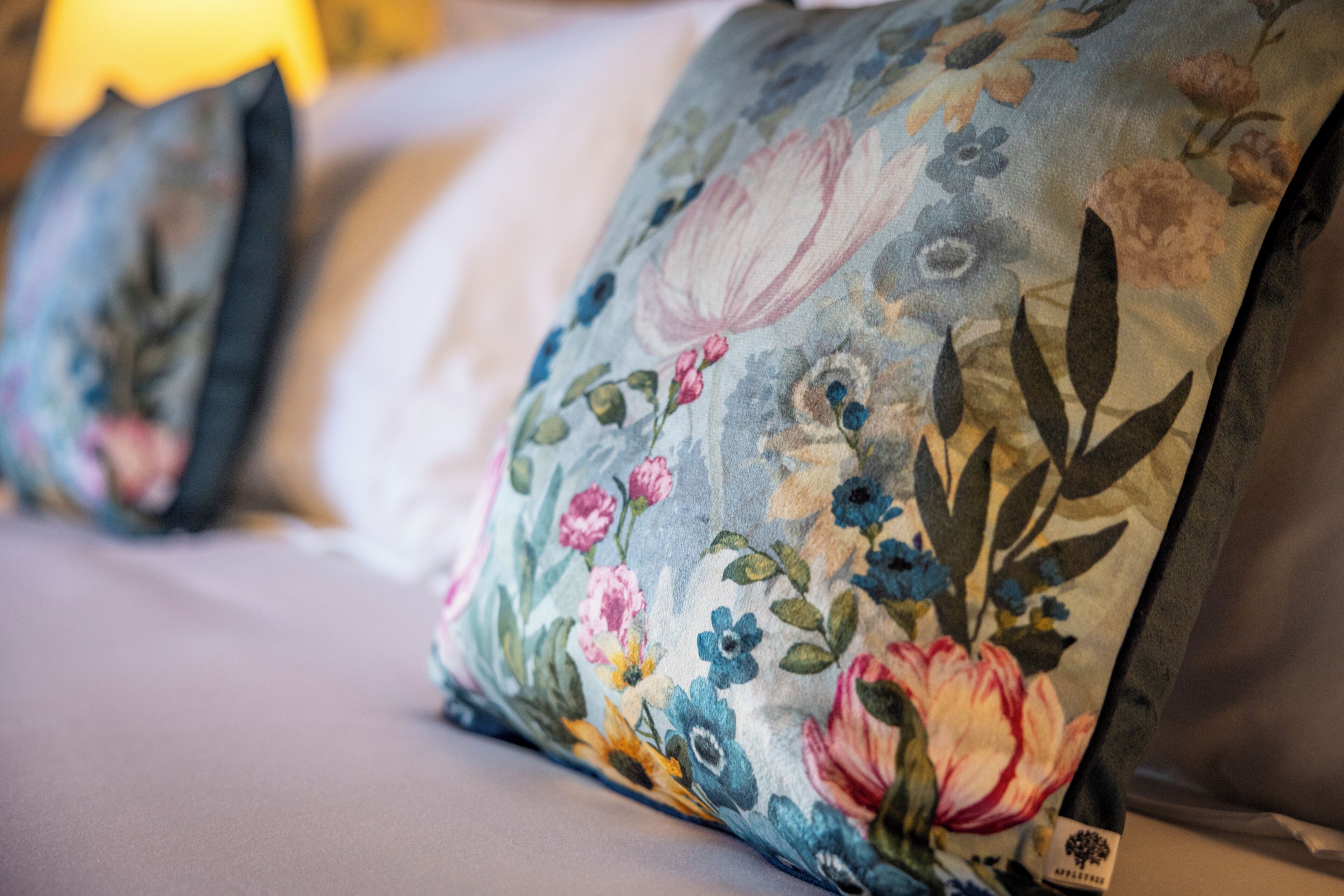 Primer plano de un cojín con estampado floral sobre una cama.
