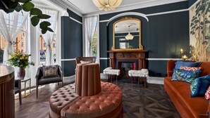 A room with a fireplace, a large mirror, a round ottoman, and a sofa with colorful pillows. - Clarence House (Londonderry)
