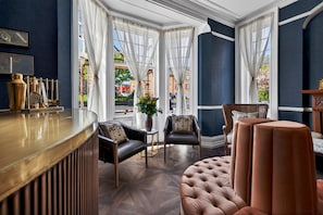 A room with a bar, two leather chairs, a tufted ottoman, and large windows with curtains. - Clarence House (Londonderry)