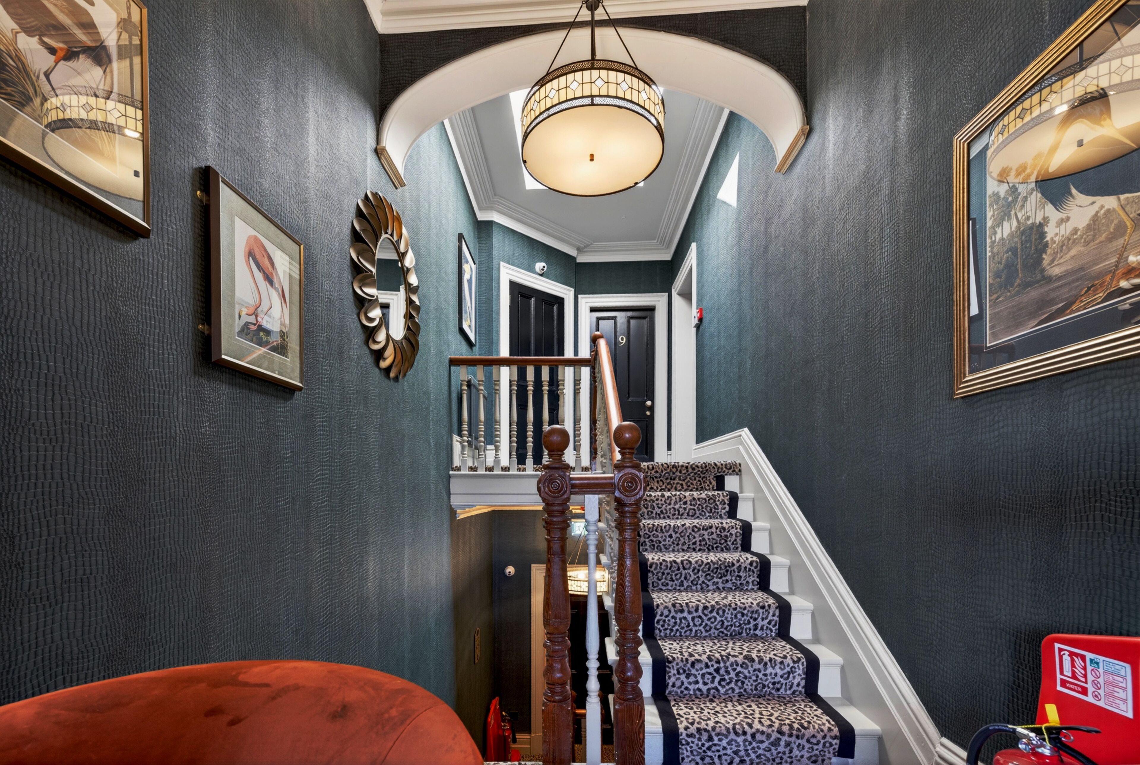 A grand staircase with a leopard print design, a chandelier, and framed artwork on the walls.