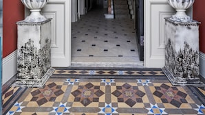 A grand entrance with a staircase, large potted plants, and a patterned floor. - Clarence House (Londonderry)
