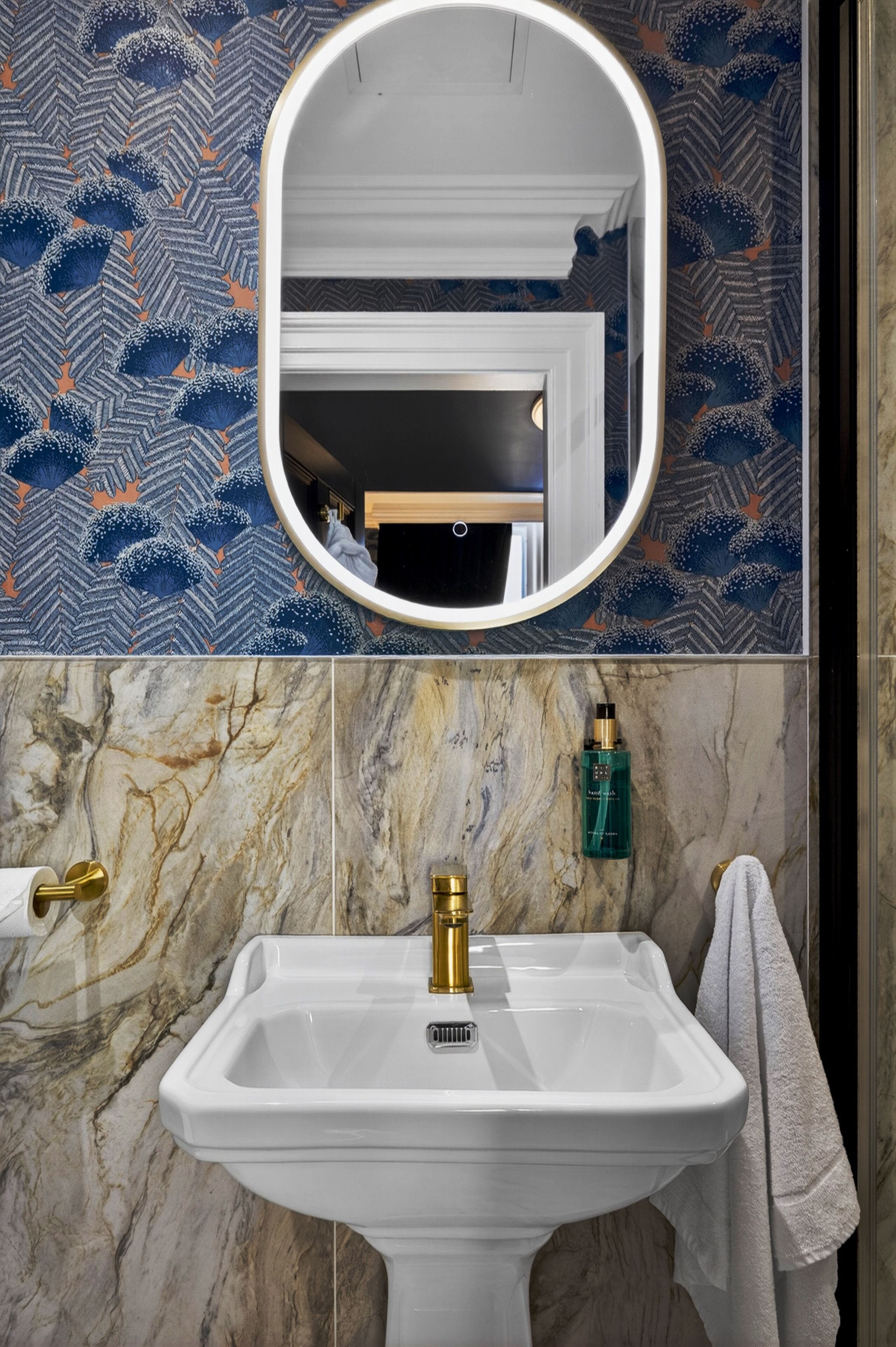 A bathroom with a white sink, gold faucet, and a mirror above it.