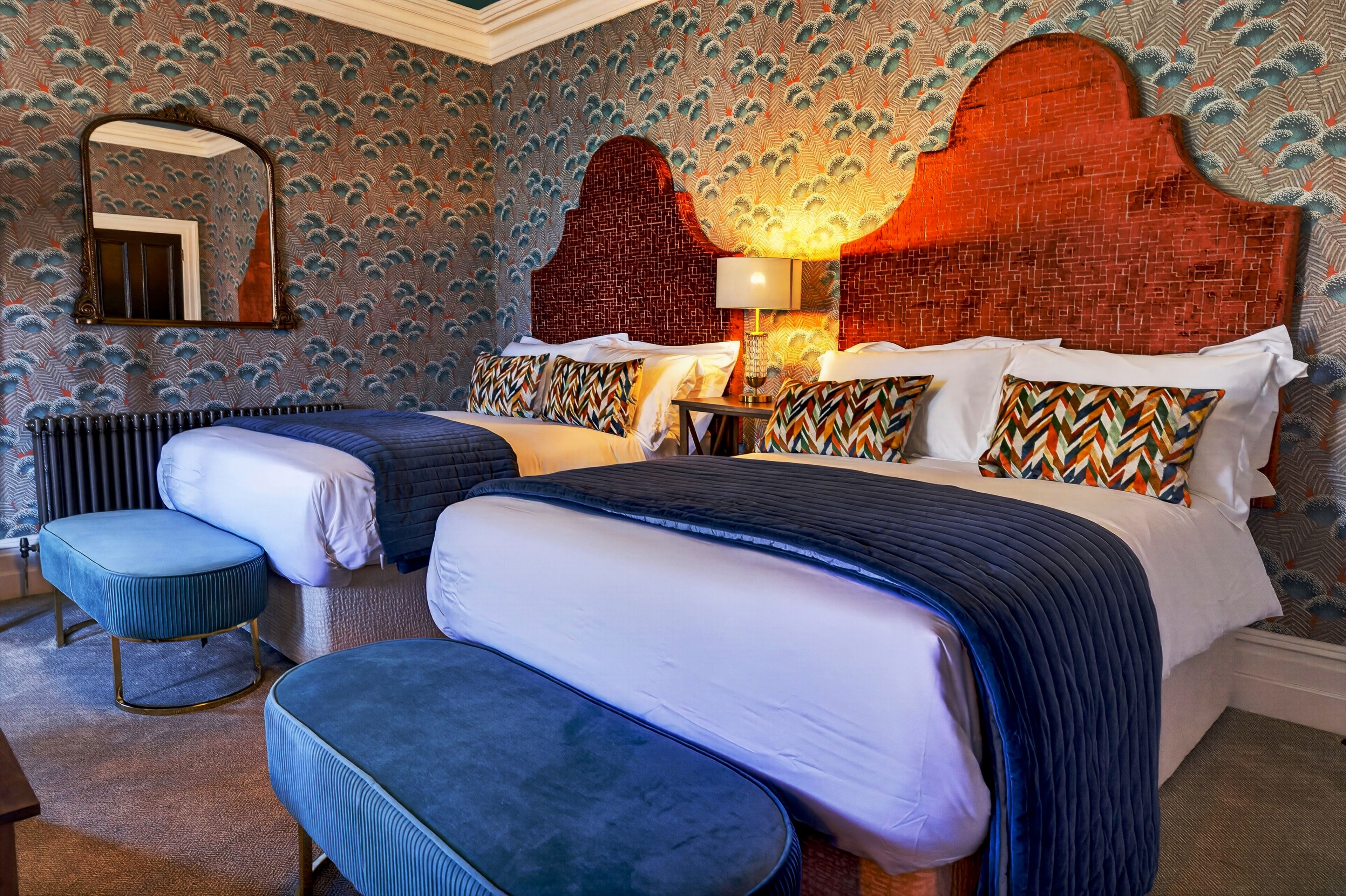 A hotel room with two beds, a large mirror, a brick-patterned headboard, and a patterned wallpaper.