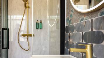 A modern bathroom with a glass-enclosed shower, a white sink with gold fixtures, and a mirror with a gold frame.