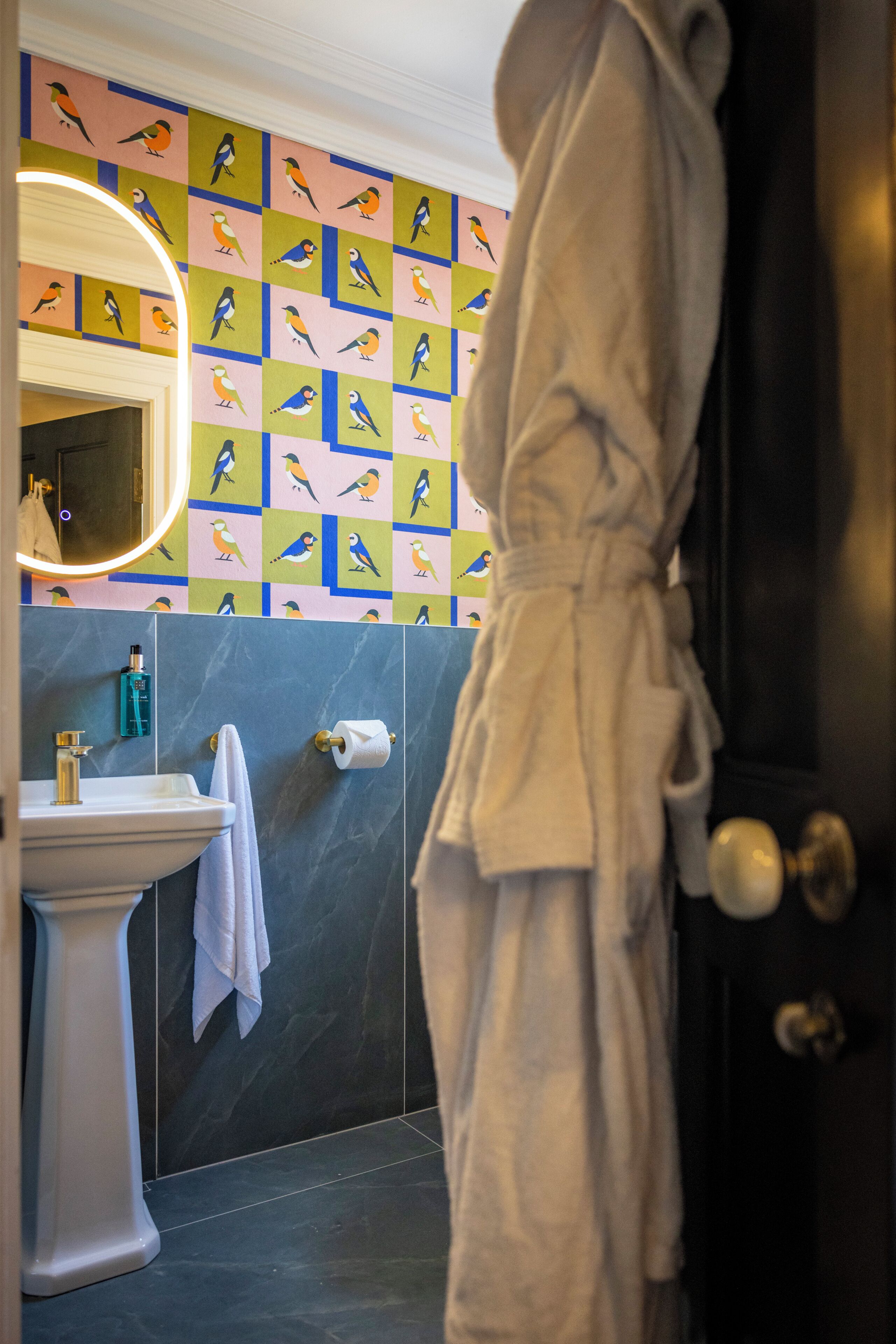 Ein Badezimmer mit Waschbecken, Spiegel, Handtuch und Bademantel, der an der Tür hängt.