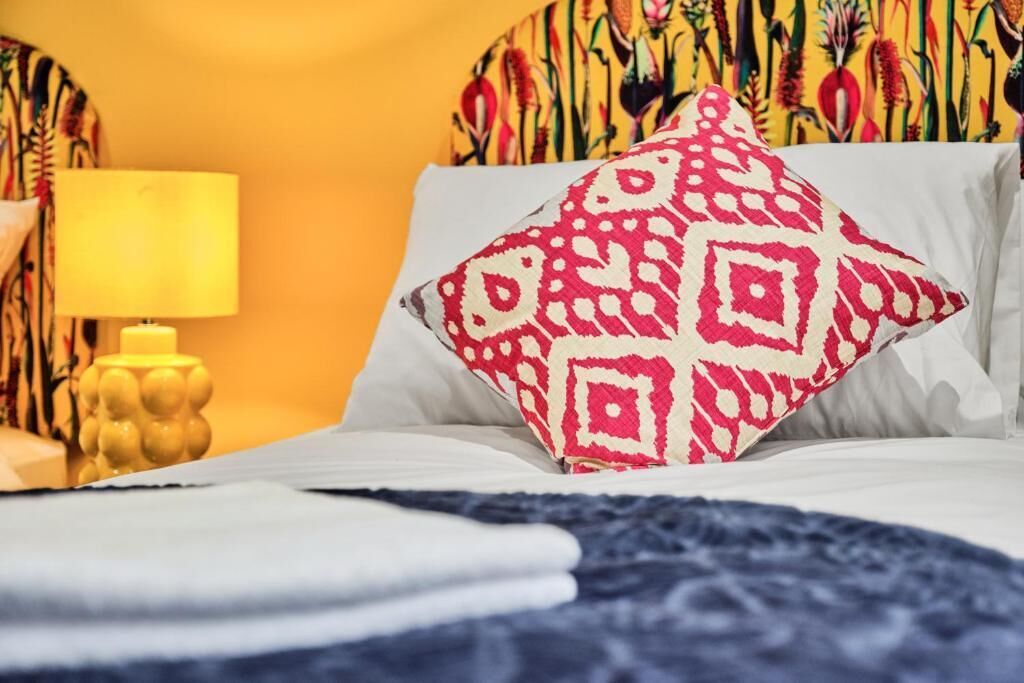 A bed with a patterned pillow, a bedside lamp, and a wall with a colorful floral pattern.