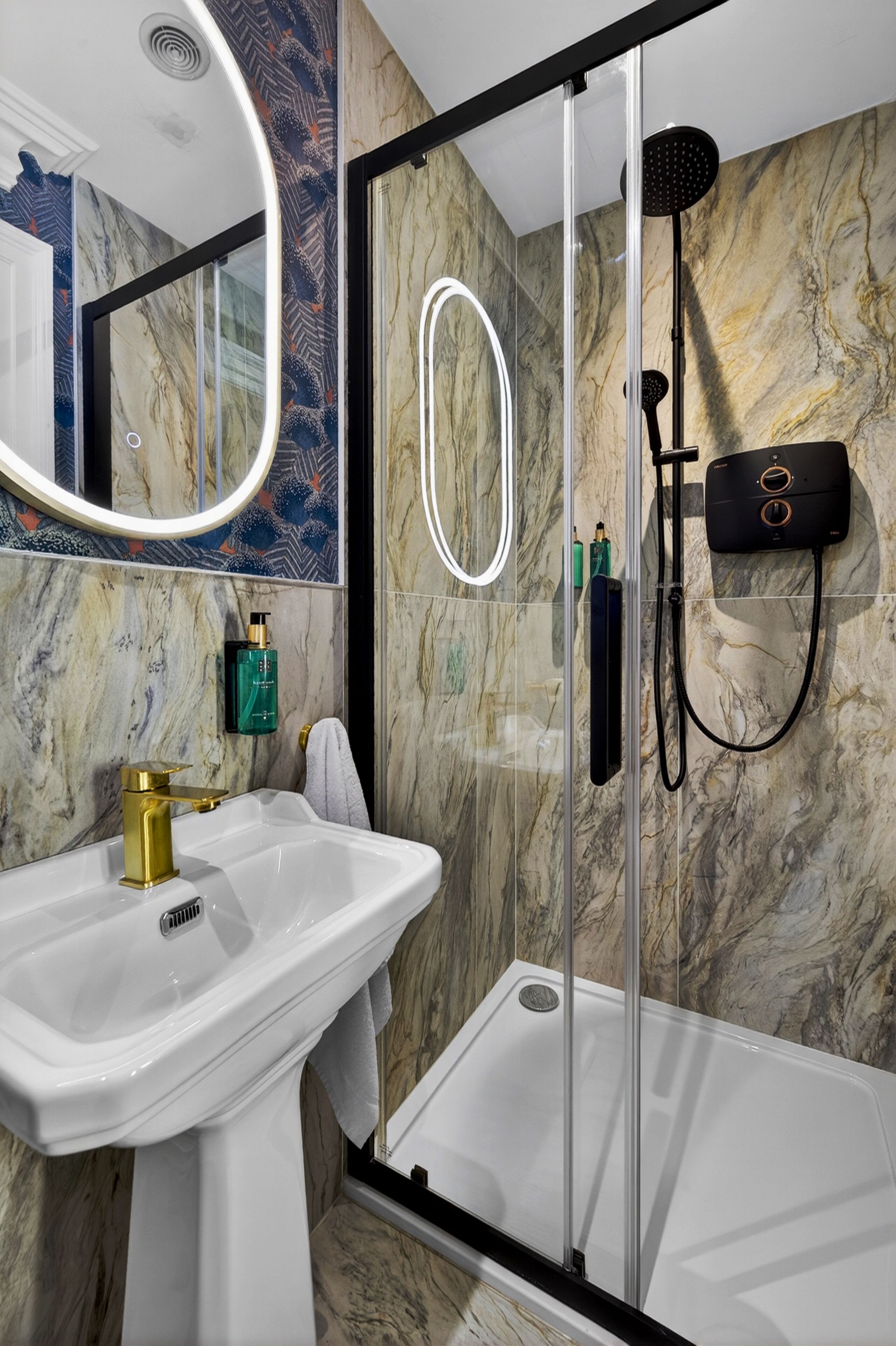 Een badkamer met een glazen douchecabine, een witte wastafel en een marmeren wand.