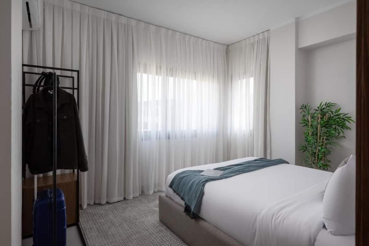 A hotel room with a bed, a plant, and a clothing rack.