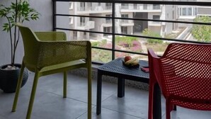 A balcony with a potted plant, two chairs, and a table with fruit. - Livingville East (New Cairo)