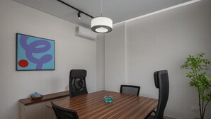 A conference room with a wooden table, black chairs, a potted plant, and a colorful abstract painting on the wall. - Livingville East (New Cairo)