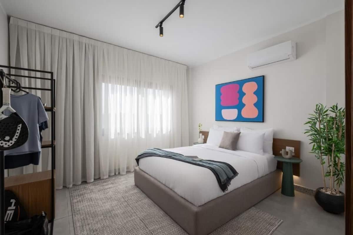 A modern bedroom with a large bed, a wardrobe, a potted plant, and a wall-mounted air conditioner.
