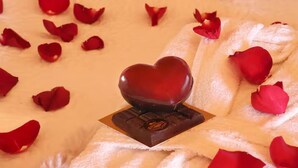 A bed with a heart-shaped chocolate box and scattered rose petals.