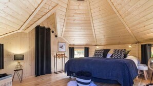 A cozy wooden cabin bedroom with a large bed, a hanging light fixture, and a view of the outdoors.