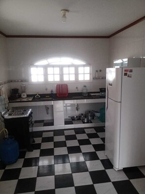 A kitchen with a black and white checkered floor, a gas stove, a refrigerator, and a window above the sink. - VACATION HOME IN ARARUAMA (Araruama)