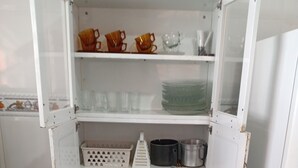 Een keuken met een witte koelkast, een geruit vloertje en planken met pannen, braadpannen en keukengerei.