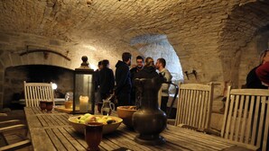 A rustic interior with a stone ceiling, wooden furniture, and a group of people gathered around a table with food and drinks. - Le Grand Gîte Renaissance au Château (12 pers.) - Lot (Saint-Chamarand)