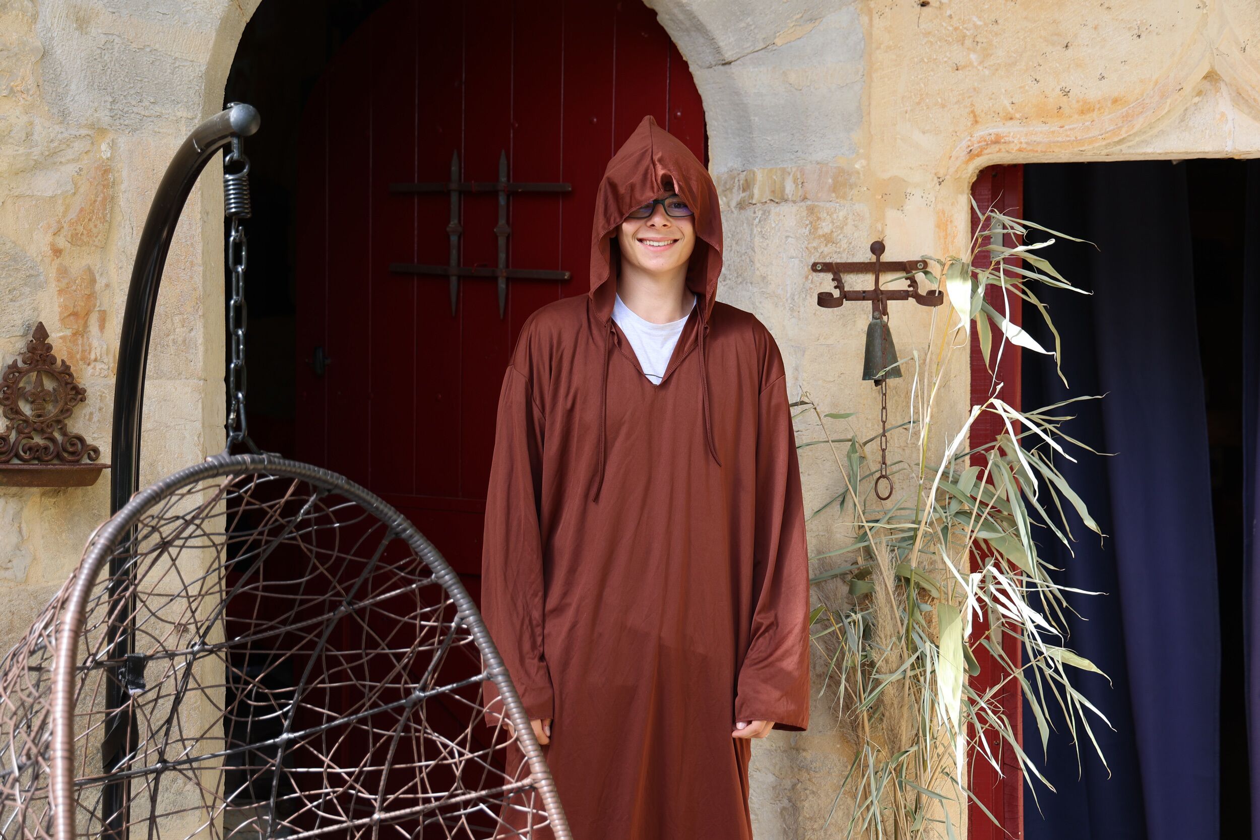 A person standing in front of a red door with a metal gate, a bell, and a plant.
