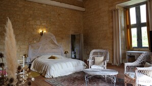 A bedroom with a stone wall, a bed with a canopy, wicker chairs, and a desk. - Le Grand Gîte Renaissance au Château (12 pers.) - Lot (Saint-Chamarand)