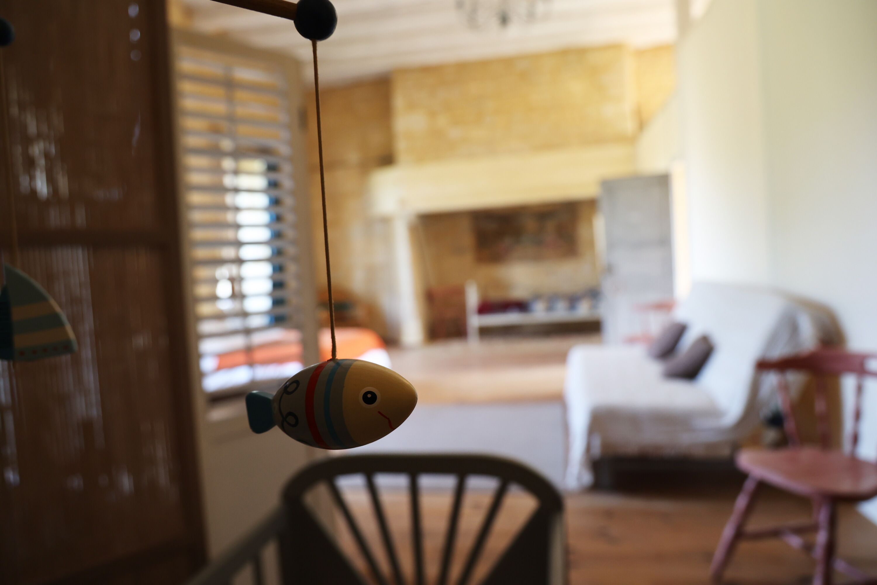 Um quarto com uma cadeira de madeira, um brinquedo pendurado e uma lareira ao fundo.