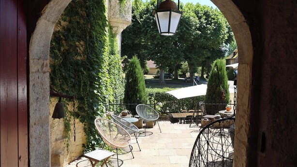An outdoor patio area with stone flooring, wicker chairs, and a hanging lantern. - Le Grand Gîte Renaissance au Château (12 pers.) - Lot (Saint-Chamarand)