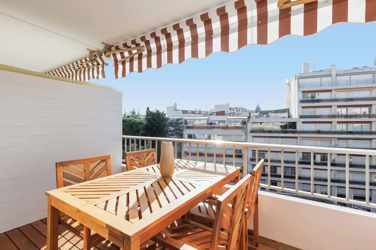 Un terrazzo in legno con tavolo e sedie, affaccia su una vista panoramica della città con edifici moderni.