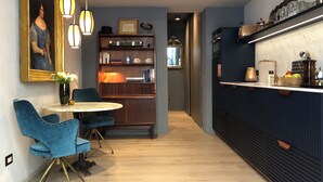 Een moderne keuken met een houten vloer, een eethoek met een blauwe stoel en tafel, en een boekenkast met diverse spullen.