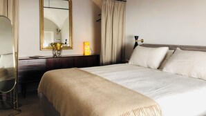 Een hotelkamer met een groot bed, een nachtkastje met een lamp, een spiegel en een dressoir.