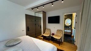 Ein modernes Schlafzimmer mit einem großen Bett, einem Fernseher, zwei Sessel und einem Spiegel.