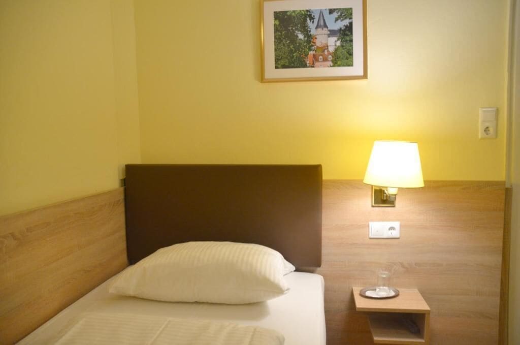Una habitación de hotel con una cama, una mesita de noche, una lámpara y un cuadro en la pared.