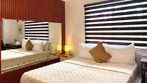 Ein Hotelzimmer mit einem großen Bett, einem Nachttisch mit Lampen, einem Spiegel und gestreiften Vorhängen.