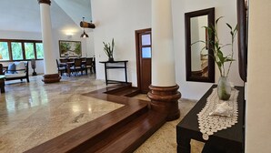 Un hall d’entrée spacieux avec un plafond haut, de grandes colonnes, un sol en marbre et un espace détente avec des fauteuils et des tables.