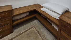 Une chambre d’angle avec un lit superposé en bois, une petite commode en bois et un portant à vêtements.