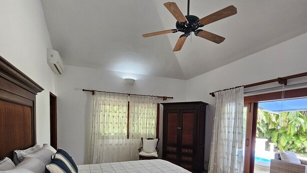 Une chambre à coucher avec un lit, un ventilateur de plafond, une fenêtre avec des rideaux et une vue sur l’extérieur.