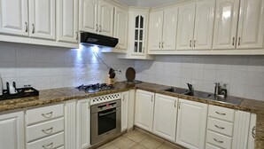 Une cuisine avec des meubles blancs, une cuisinière à gaz, un four et un évier.