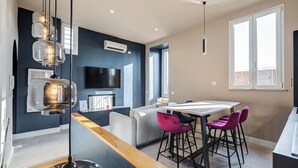 A modern kitchen with a dining area, a TV mounted on the wall, and a large window providing natural light. - VIVILO COLLECTION - Vivilo Roma Trevi (Terrace+Jacuzzi) Close to Trevi Fountain (Roma)