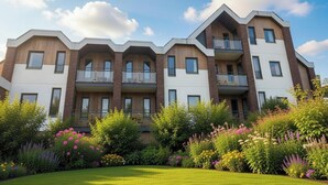 A multi-story residential building with balconies, surrounded by a well-maintained garden with various flowering plants. - Couple Stay at Hambachtal Holiday Park (Oberhambach)