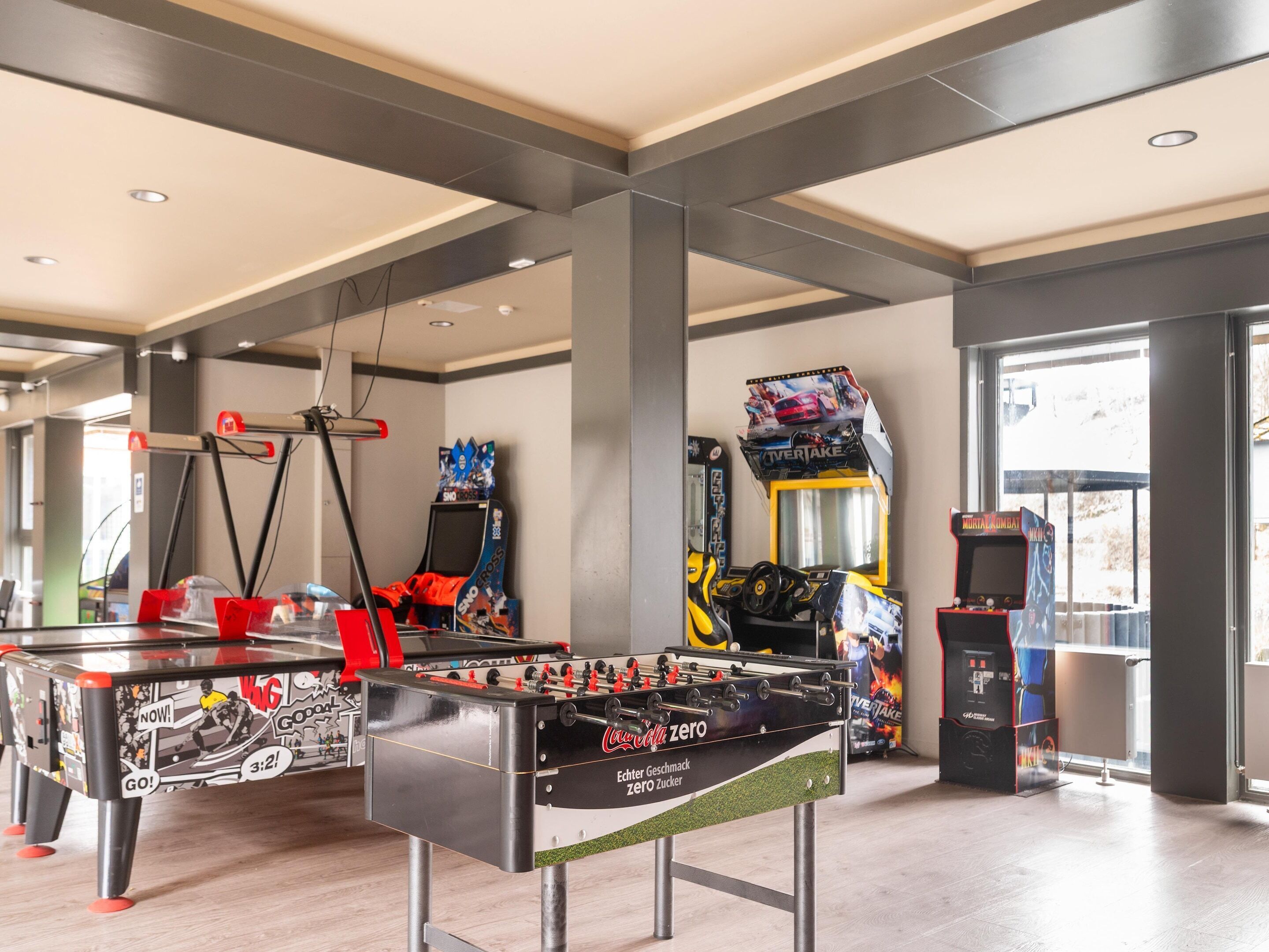 Un grand espace intérieur comprenant une table de baby-foot, des jeux d’arcade et une grande fenêtre laissant entrer la lumière naturelle.