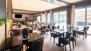 A spacious dining area with multiple tables and chairs, large windows, and a flat-screen TV mounted on the wall. - Couple Stay at Hambachtal Holiday Park (Oberhambach)