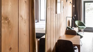 A hotel room with wooden panel walls, a bed, a desk with a chair, a green chair, and a window with curtains. - Couple Stay at Hambachtal Holiday Park (Oberhambach)