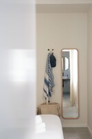 Un dormitorio con una cama, un espejo, un perchero y un cesto para guardar objetos.