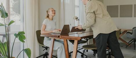 A modern office space with a large window, a laptop on a table, and a person standing by.